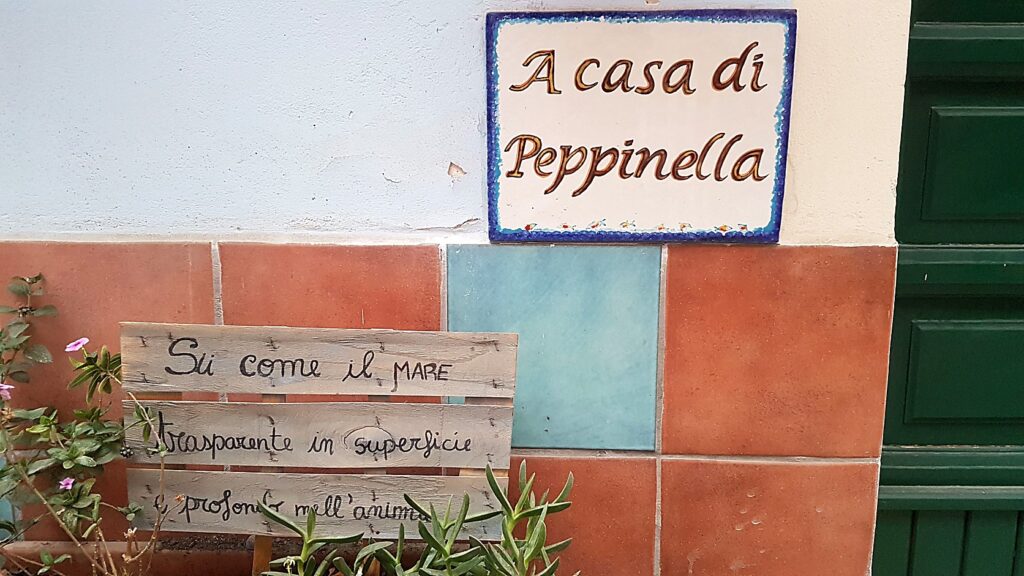 Hand-painted ceramic house sign and handwritten wooden plaque on a terracotta-tiled Italian wall