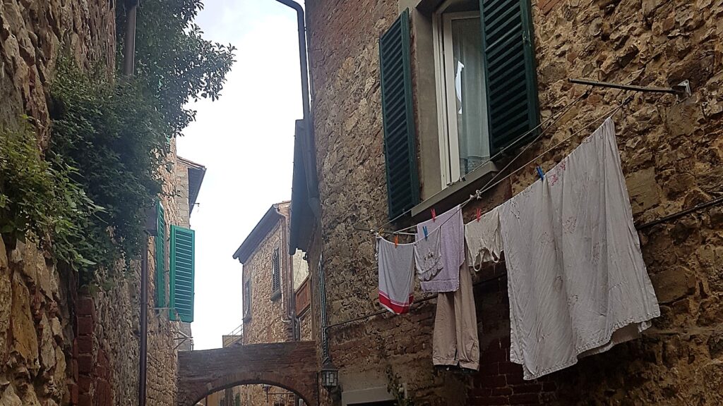 Narrow stone alley in a Tuscan hill town with green shutters and laundry hanging to dry